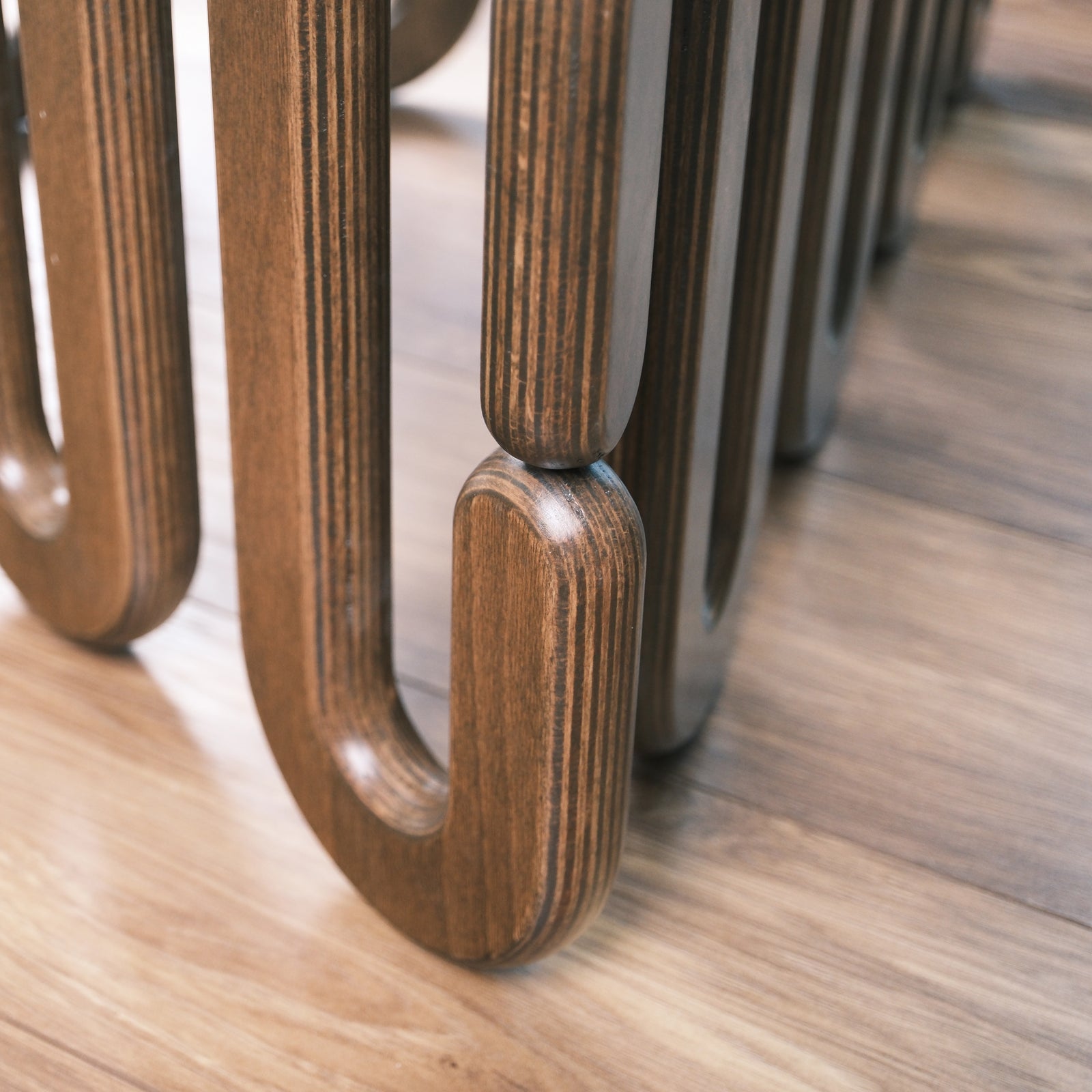 Detailansicht des geschwungenen Couchtisch-Fußes aus Schichtholz mit Glasplatte auf Teppichboden