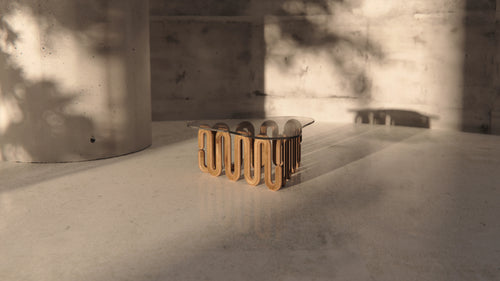 Skulpturaler Designer-Couchtisch mit geschwungener Glasplatte und organischem Holzgestell im modernen Betonambiente mit stimmungsvollem Lichteinfall