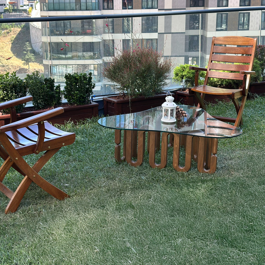 Design-Couchtisch von fofofu aus recyceltem Holz mit Glasplatte und wellenförmigem Gestell – handgefertigtes Möbelstück im modernen Gartenambiente mit Holzstühlen und Stadtblick.