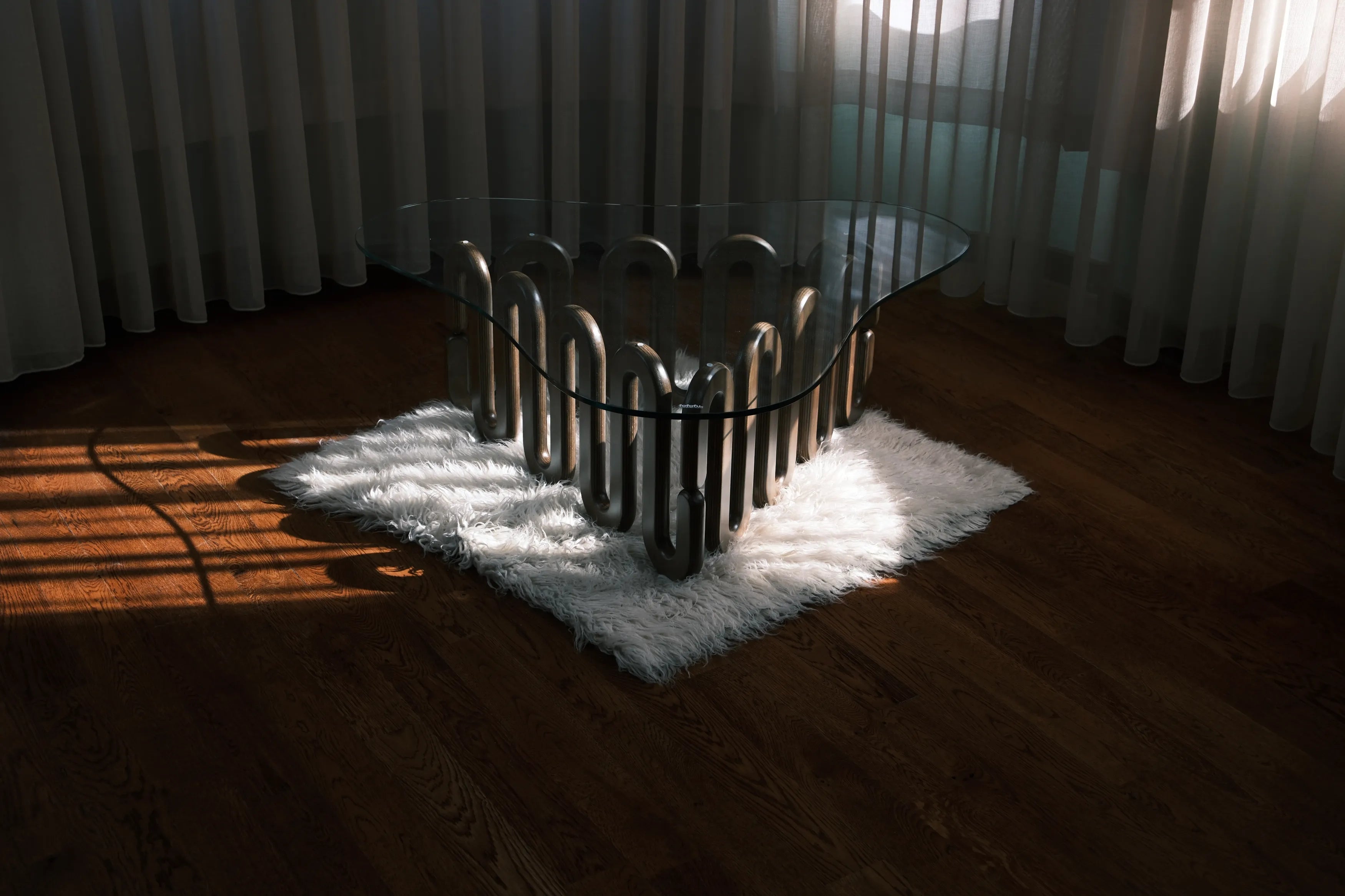 Kunstvoll geschwungener Holztisch mit Glasplatte auf weißem Teppich, modernes Design im Sonnenlicht.