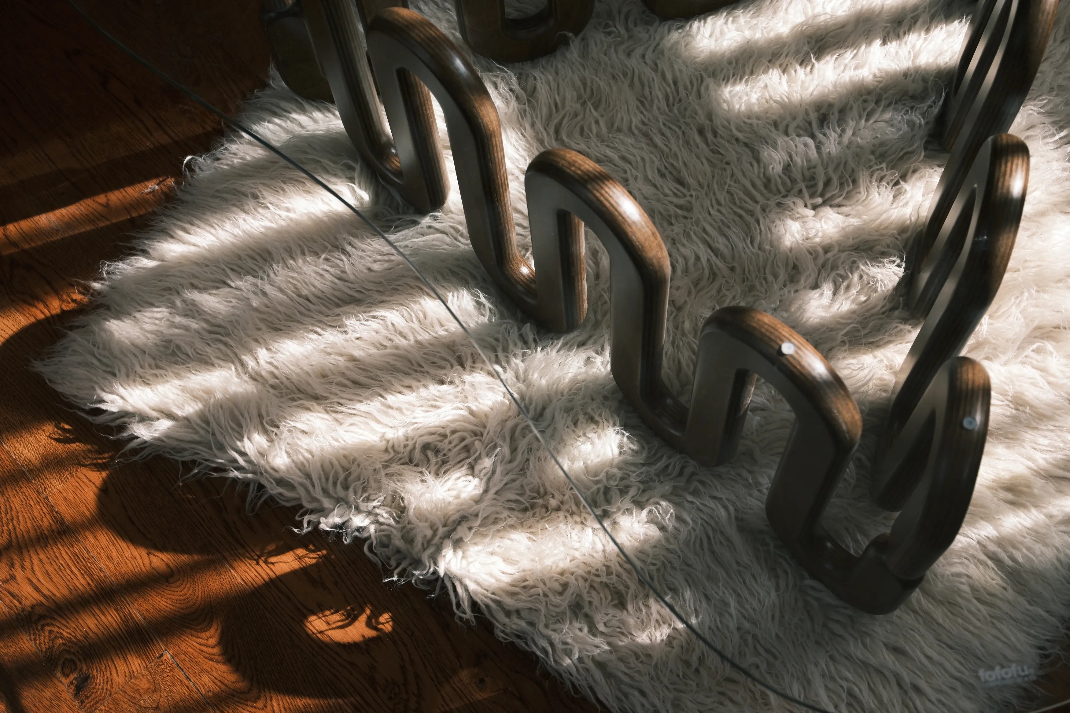Detailaufnahme eines kunstvoll geschwungenen Holzfußes mit Glasplatte auf weißem Teppich, modernes Design im Sonnenlicht auf Parkett.