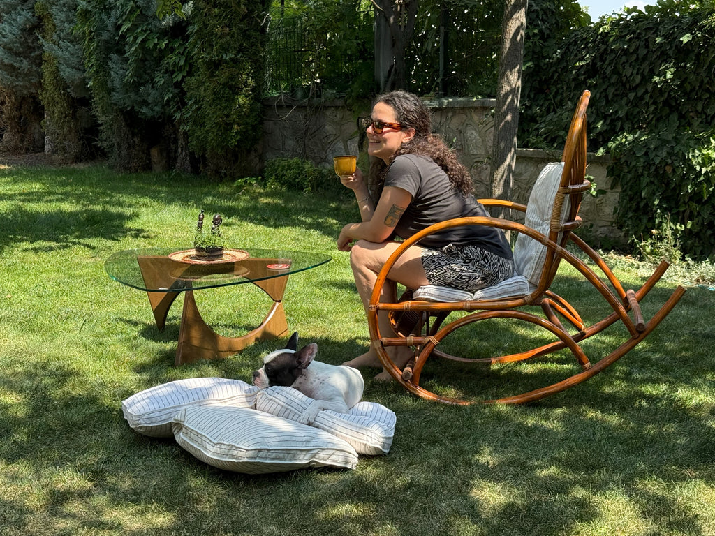 Handgefertigter Design-Couchtisch von fofofu aus recyceltem Holz mit Glasplatte – stilvolle Gartenszene mit Rattan-Schaukelstuhl, entspannter Atmosphäre und Hund auf Kissen im Schatten.