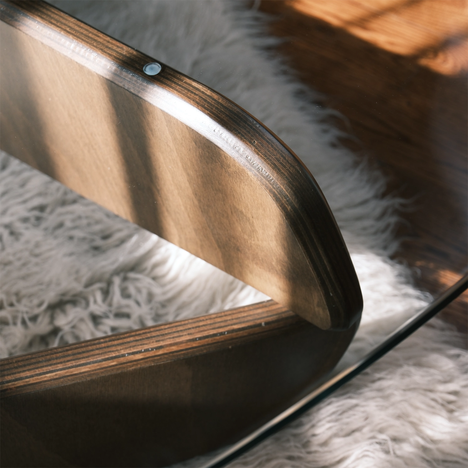 Detailansicht des geschwungenen Couchtisch-Fußes aus Schichtholz mit Glasplatte auf Teppichboden