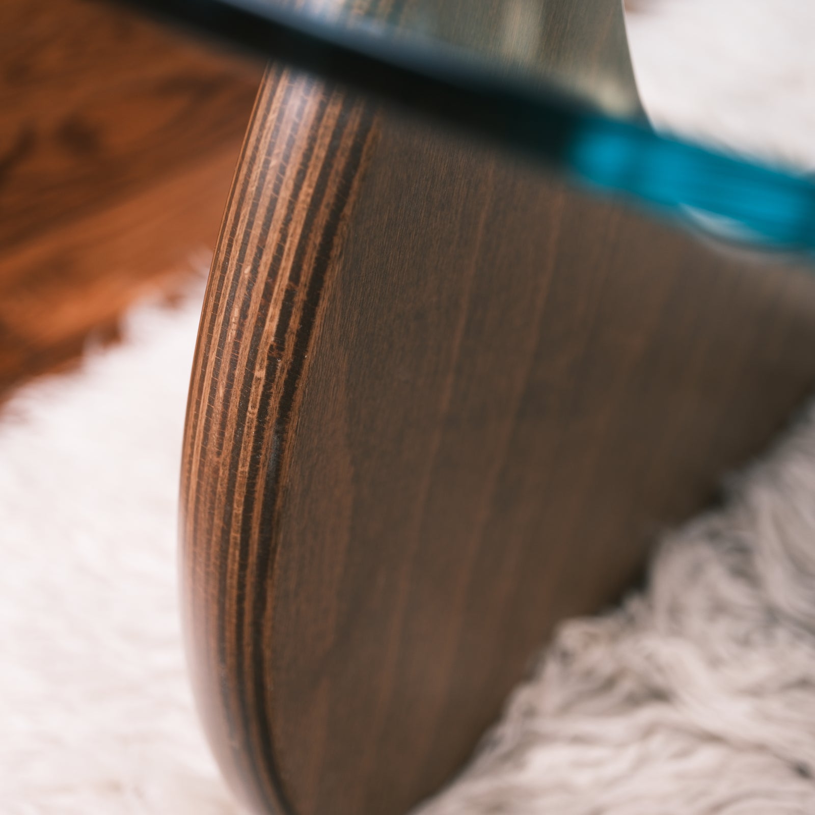 Detailansicht des geschwungenen Couchtisch-Fußes aus Schichtholz mit Glasplatte auf Teppichboden